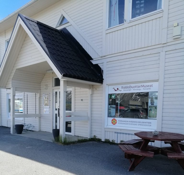 Porsanger Museums fasade mot Torget. Sommer, solskinn og benk.