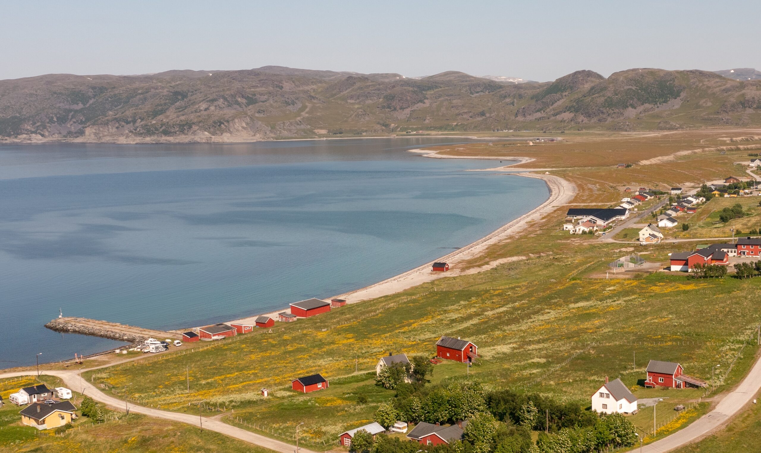 Dronebilde over kokelv, man ser bebyggelsen, og museet nederst til venstre. sommerbilde, sol, fjord, fjæra
