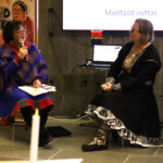 Two Sámi women in traditional clothing sitting and discussing.