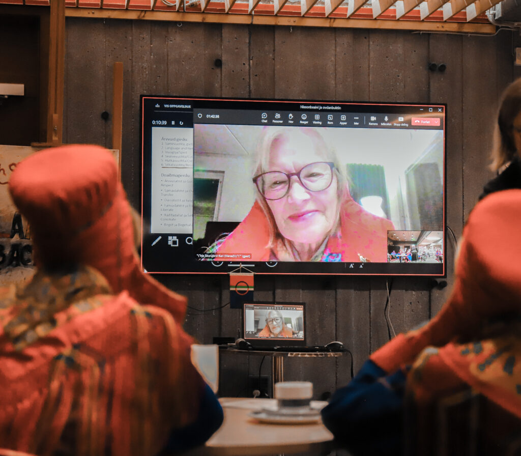 a Sámi woman in traditional clothing having a speech through a TV screen.